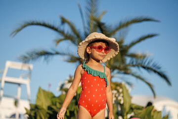 Funny little girl relaxing on summer vacation. The child has fun on the beach. Cute baby in a colorful swimsuit and sunglasses is resting.