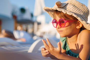 Funny little girl relaxing on summer vacation. The child has fun on the beach. Cute baby in a colorful swimsuit and sunglasses is resting.