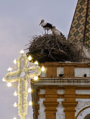 Cross illuminated with bulbs above stork nests in Carrion, Seville
