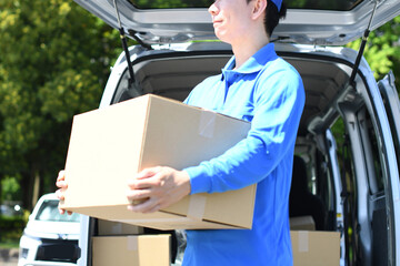 軽バンの前で荷物を運ぶアジア人男性配達員