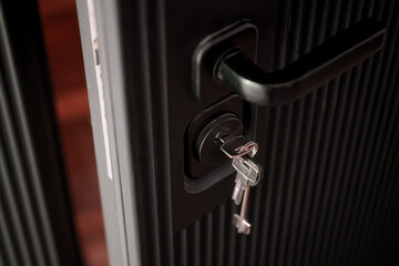Close-up of a black armored door slightly ajar showing keys in the lock and a dark interior beyond, evoking mystery and suspense. Photo. Selective focusing. High resolution