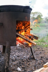 Fire Burns Brightly in a Rustic Metal Stove While Wood is Added for Cooking Outdoors in a Natural...