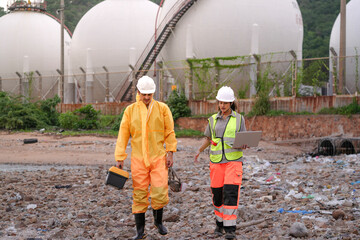 Two environmental researchers walk back from shoreline testing. They carry safety gear, a toolbox, a respirator mask, and a laptop after collecting water samples from a contaminated coast.