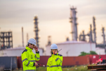 Two engineers in high-visibility safety gear and helmets conduct a field inspection at an...