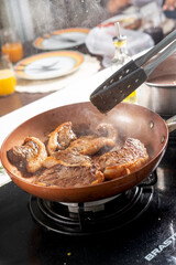Chef cooking steaks on a frying pan in a restaurant kitchen