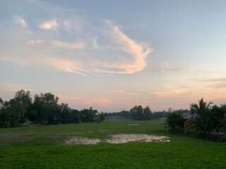 Peaceful rural landscape at sunset with lush green fields and soft clouds
