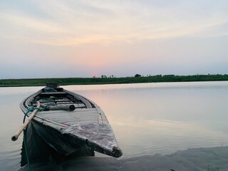 Old wooden boat rests on sandy shore at sunset with calm water reflection