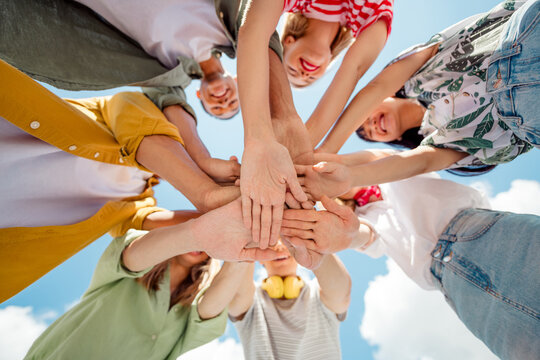 Happy young individuals uniting hands in celebration outdoors under a bright summer sky showcasing teamwork