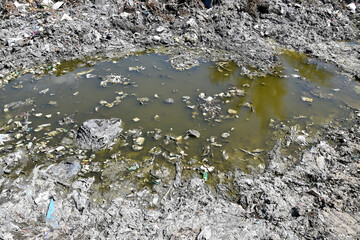 polluted stagnant water puddle in garbage dump area under sunlight, urban environmental pollution
