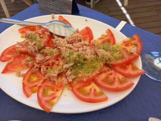 Fresh tomato and tuna salad with herbs on white plate setting for dining experience. Mediterranean...