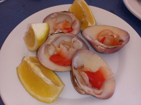 Fresh clams with lemon wedges on white plate - seafood dining experience. Callista chione, concha fina