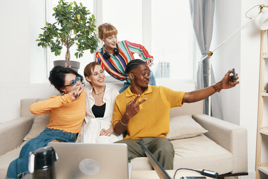 Young adult man taking selfie with colleagues and friends socializing in casual workplace setting, showcasing Gen Z teamwork and modern business interaction. - Powered by Adobe