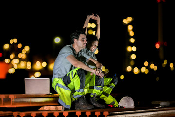 Two industrial workers take a break during the night shift at a construction site, sitting on steel...