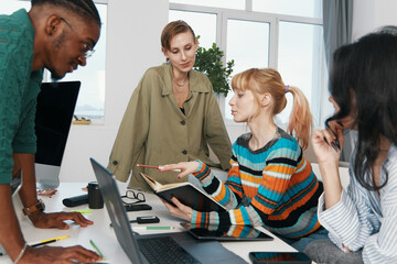 Young adult woman collaborating with colleagues in modern workplace, discussing work project and...