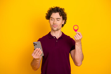 Young man with curly hair using smartphone and holding pink marker against vibrant yellow...