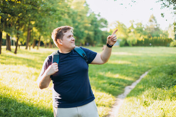 One Caucasian male hiking in the woods in summer. Travel, active lifestyle, people and hobby concept. Blonde male in sport clothes pointing finger outdoors. Traveler enjoys eco-tourism