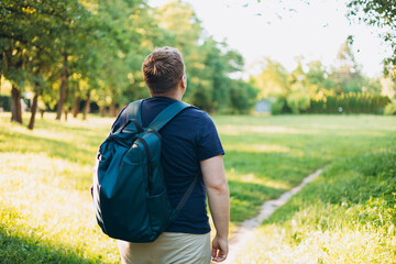 Rear view of blonde man with backpack standing in the countryside. Traveler. Summer time. Portrait of happy young man in casual clothing standing outdoor