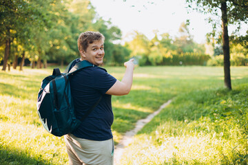 One Caucasian male hiking in the woods in summer. Travel, active lifestyle, people and hobby concept. Blonde male in sport clothes pointing finger outdoors. Traveler enjoys eco-tourism, rear view