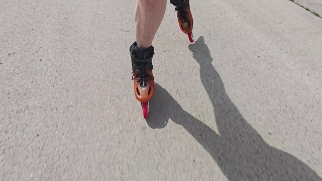 Close-up view of male legs in orange inline blades boots moving on the road. 