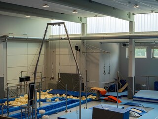 Modern gymnastics gym with training equipment: rings, pommel horse, parallel bars, mats, and foam pit. Indoor sports facility for physical education and acrobatics