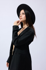 A stylish brunette woman in a wide-brimmed black hat poses against a light background