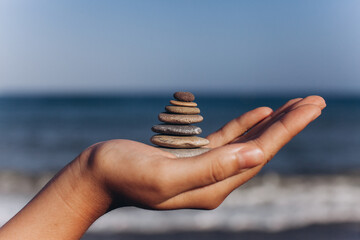 Hand holding stack of zen stones at the beach