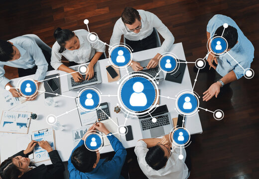 A top-down view of a diverse group of professionals collaborating around a table with laptops, discussing data, and engaging in networking strategies for effective teamwork. Amity - Powered by Adobe