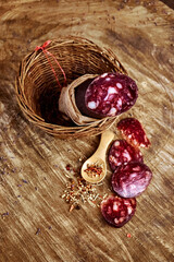 Village still life with a piece of smoked sausage in a fabric casing in a basket, sausage slices and a spoon with spices. Home cooking, natural product.