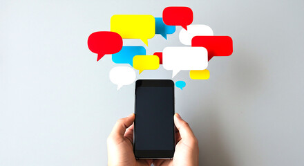 Hands holding smartphone with colorful speech bubbles floating above on a gray background view from above