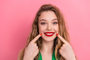 Happy young woman with braces smiling and pointing at her teeth against a pink background