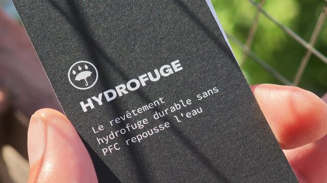 Hand showing a card explaining that the waterproof and durable coating without PFC repels water, in French
