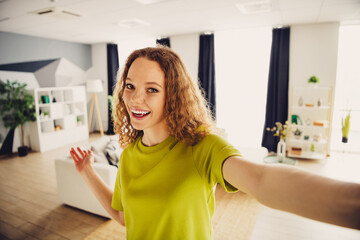 Positive woman with curly red hair enjoying a comfortable and stylish moment in a modern living...