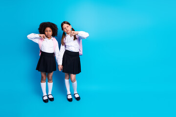 Fototapeta premium Two young schoolgirls in uniform express contrasting emotions on a bright blue background, symbolizing diversity and friendships