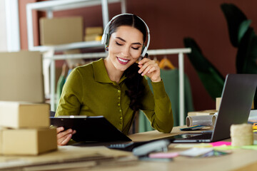 Young female entrepreneur working remotely with a laptop and packages in a fashion atelier office...