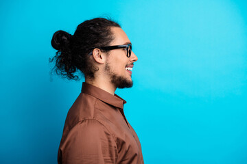 Young man in profile smiling confidently against a vibrant blue background wearing stylish brown...