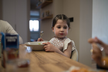 Little girl eating soup at the table with family
