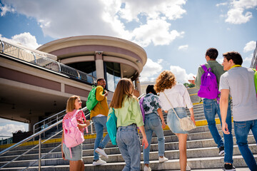 Group of youthful friends bonding outdoors on a sunny day, ascending steps with vibrant backpacks...