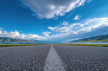 Fototapeta premium Asphalt road leading to a distant lake and mountains under a partly cloudy sky