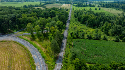 Aerial view captures an abandoned railway stretching through vibrant green fields and dense woodlands. The tranquility of the rural setting is highlighted by the surrounding foliage.
