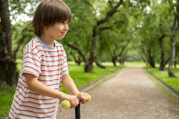 Little boy is riding on scooter. Child is playing in the park in summer day. Healthy outdoor activity. Cute kid is on his way to school.