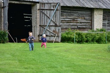 Toddler boy walking outdoors with a rake in one hand and rubber shoes in another in countryside....
