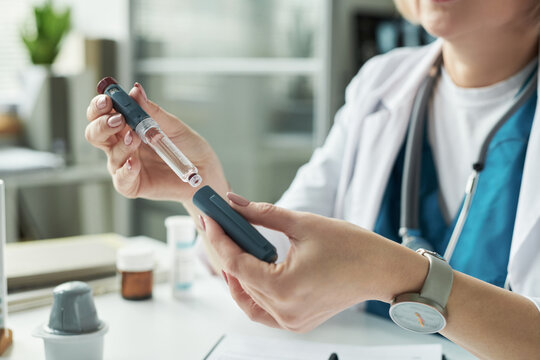 Caucasian middle aged female doctor preparing insulin injection for diabetes treatment in medical office, holding insulin pen and vial while explaining medication usage to patient