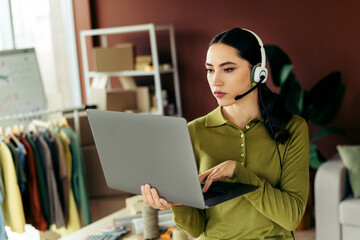 Young woman with headphones working on a laptop in a creative fashion studio office workspace