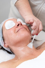 Beautician applying cream on woman's neck with brush during skincare treatment