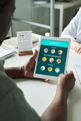 Middle aged Black man holding digital tablet displaying diabetes dietary recommendations during...
