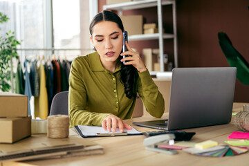 Young entrepreneur working in a modern atelier setting, discussing fashion business on the phone...
