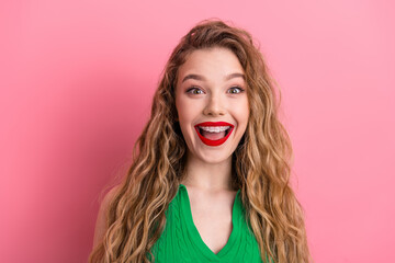 Joyful young woman in a green top with long blonde hair and braces smiling brightly against a...