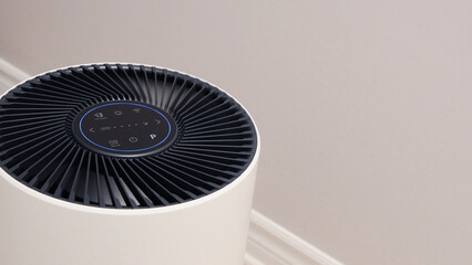 Tall round air purifier with a black top fan and a white body on a tile floor against the wall