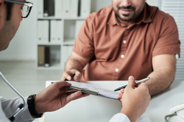 Middle aged Caucasian man consulting doctor in medical office, discussing diabetes management while holding clipboard and pen, hands and partial faces visible, healthcare concept