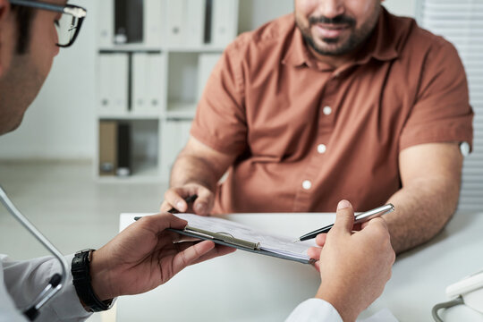 Middle aged Caucasian man consulting doctor in medical office, discussing diabetes management while holding clipboard and pen, hands and partial faces visible, healthcare concept